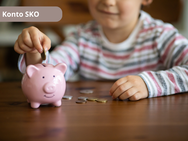 Dziewczynka siedzi przy stole i wrzuca monety do świnki skarbonki